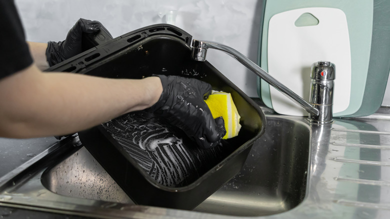 Person's gloved hand scrubbing air fryer basket