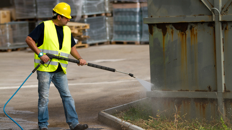 Man using a powerful pressure washer on a metal container