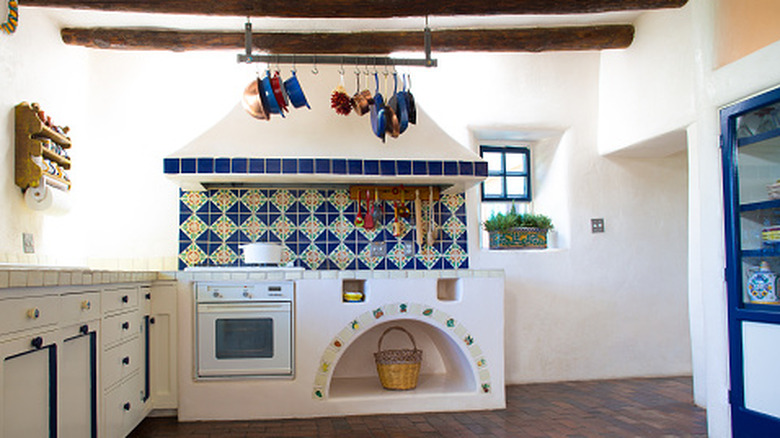 A rustic, Southwestern-style kitchen with wooden beams, white walls, and a colorful backsplash