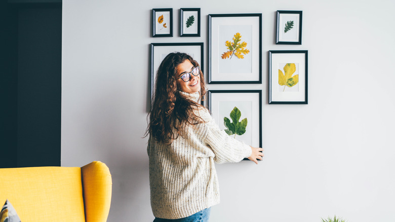 A person hanging a framed leaf as part of a gallery wall