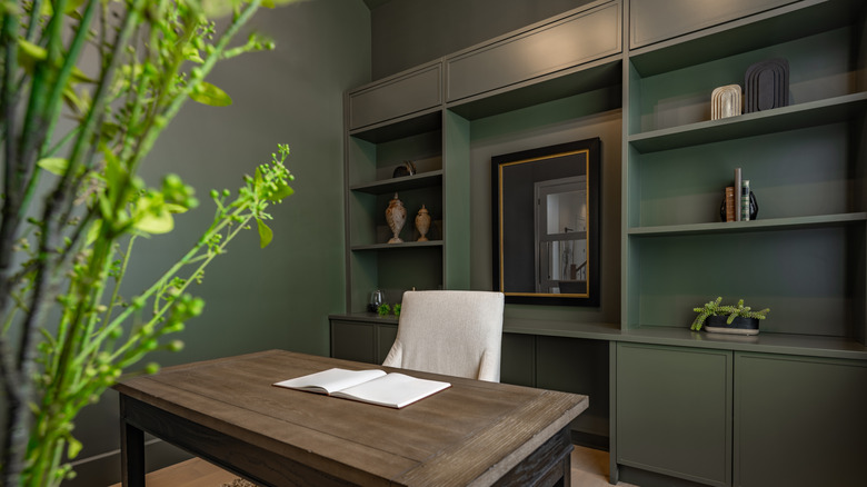 Home office with a desk, upholstered chair, and built-in bookshelves entirely painted in deep forest green all around