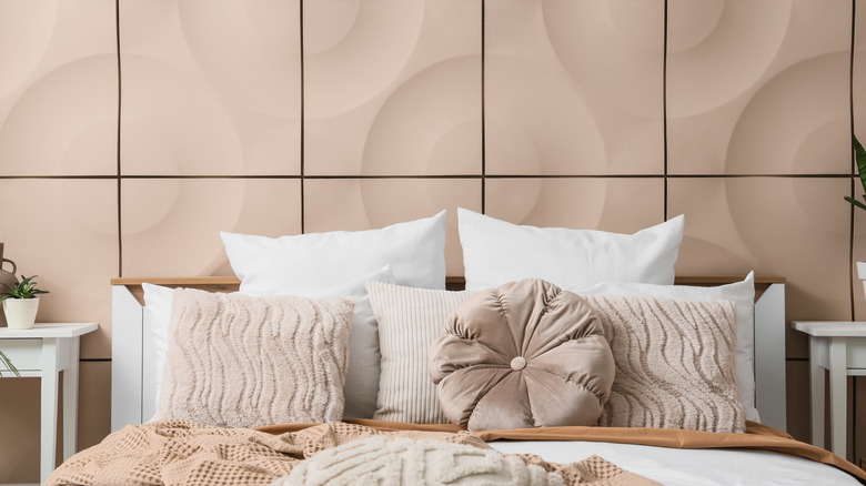 Freshly made bed with throw pillows set against a soft pinkish-beige tiled wall in a bedroom