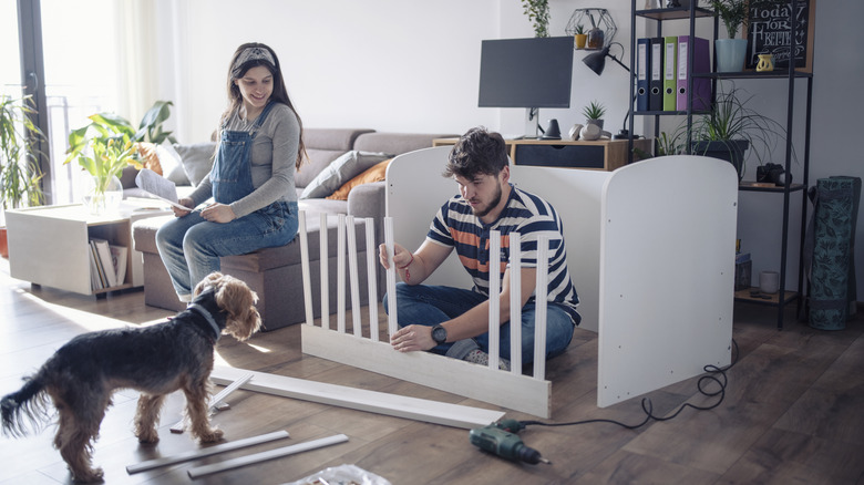 A woman watches as a man puts together a crib