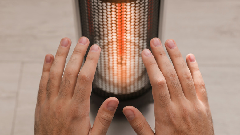 A man warms his hands in front of a heater