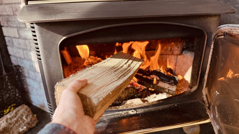 A hand puts a chopped log into a wood-burning stove.