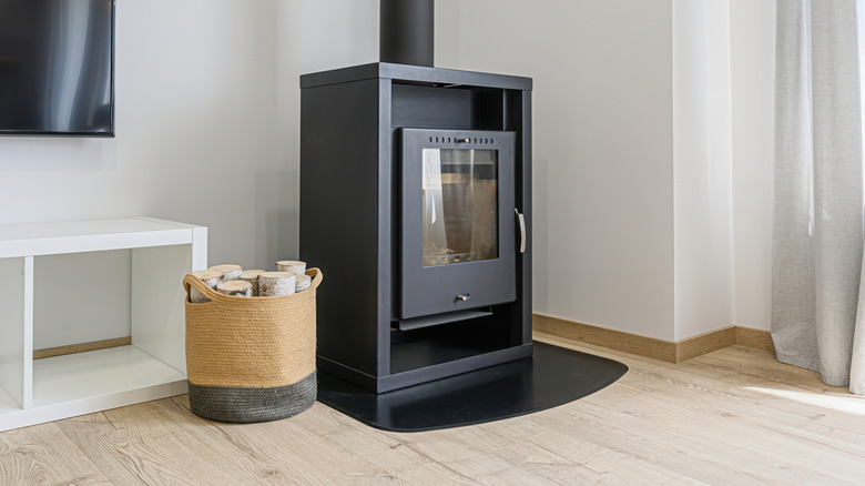 An unlit wood burning stove in a minimalist living room with a basket of firewood beside it..
