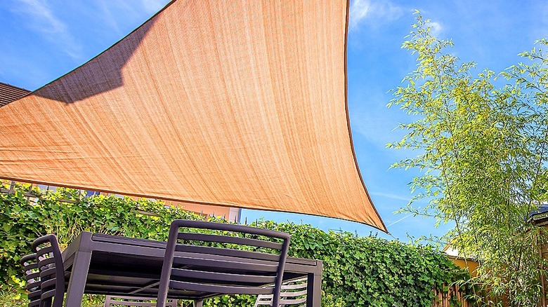 A shade sail is seen above an outdoor dining table set in a backyard with a blue sky