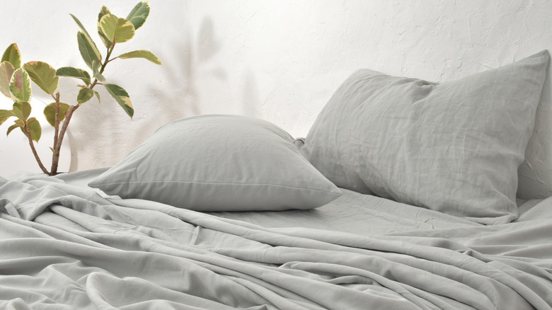 grey linen sheets on a bed with plant in the background