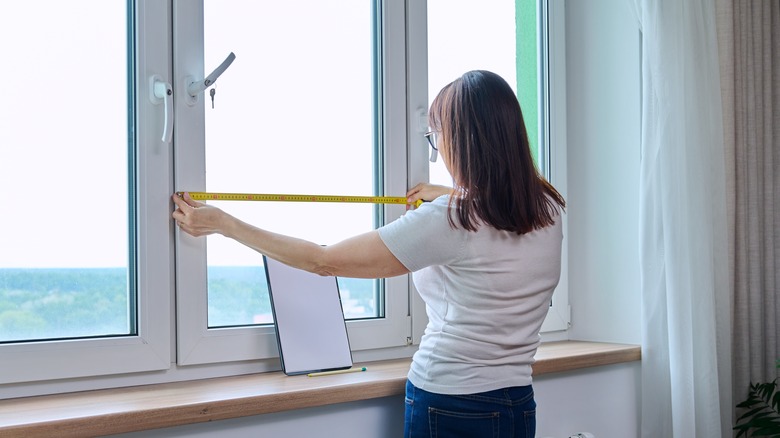 A person measures a window