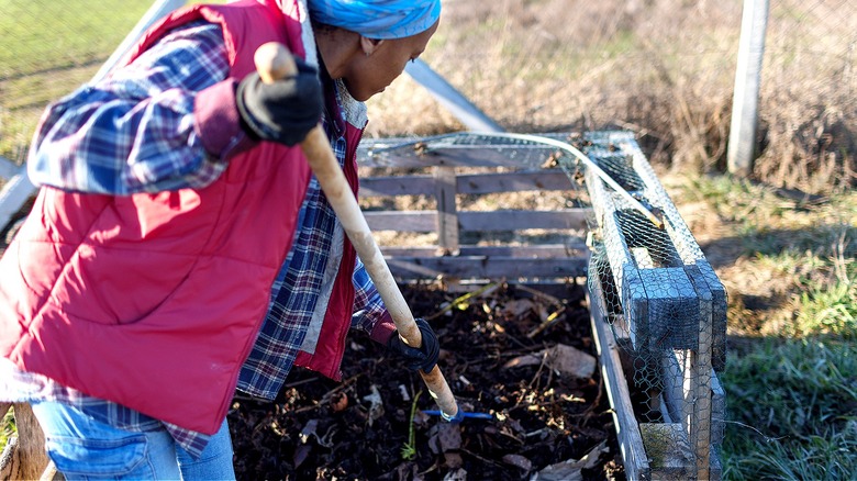 A person uses a compost fork to turn over their compost pile