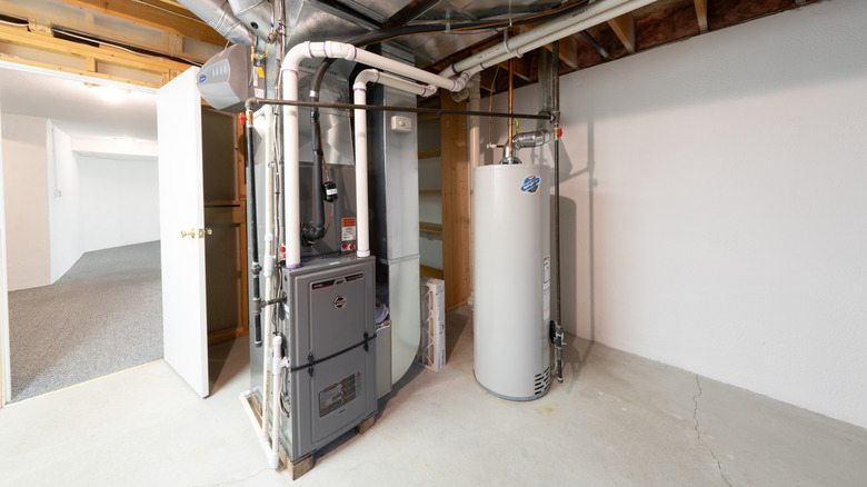 A water heater stands awkwardly by a home furnace in a finished basement.