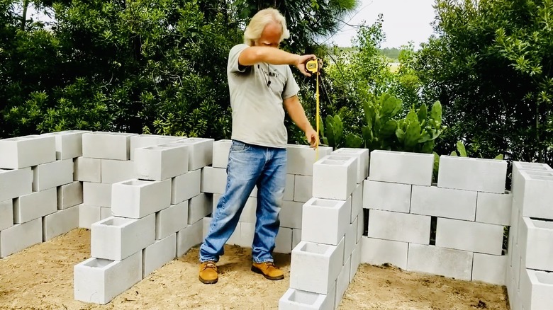 Man measures height of concrete compost bin he has built.