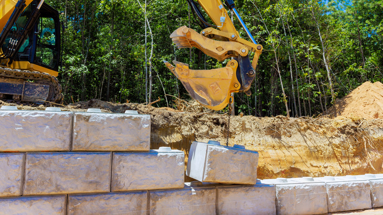 Construction work with an excavator moving heavy stone blocks under build sturdy retaining wall.