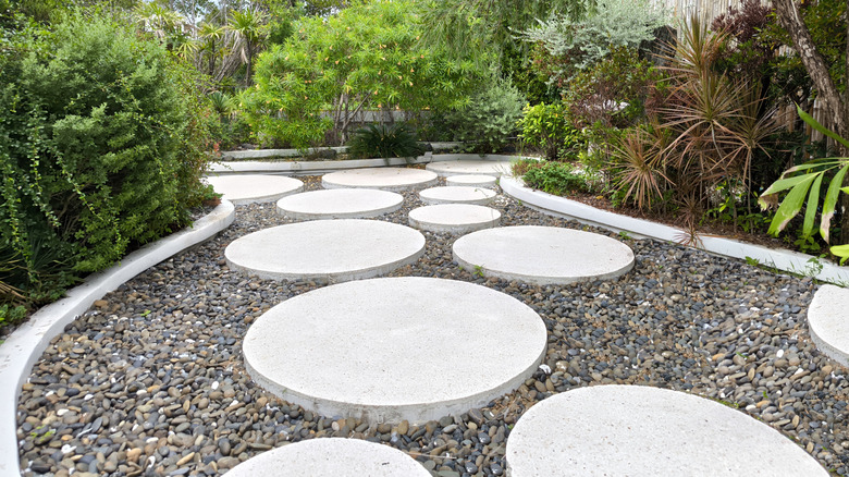 A garden with a gravel pathway with large cement stepping stones on top