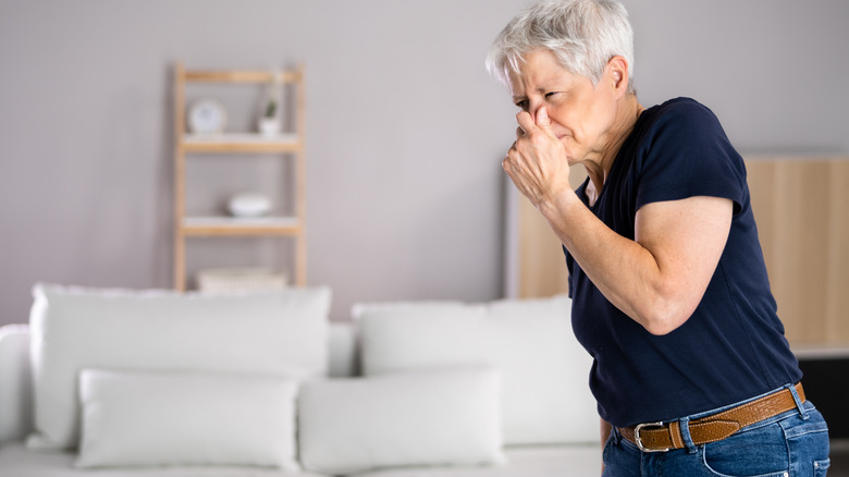 Old woman holds her nose indicating a bad smell in the house