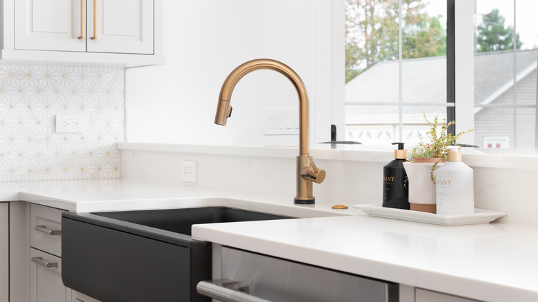 Black sink with gold faucet in white kitchen