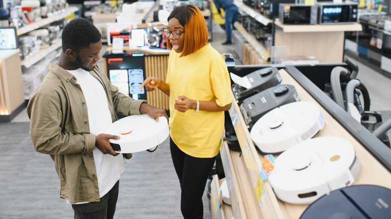 a young couple buying robotic vacuum cleaner in an appliances store
