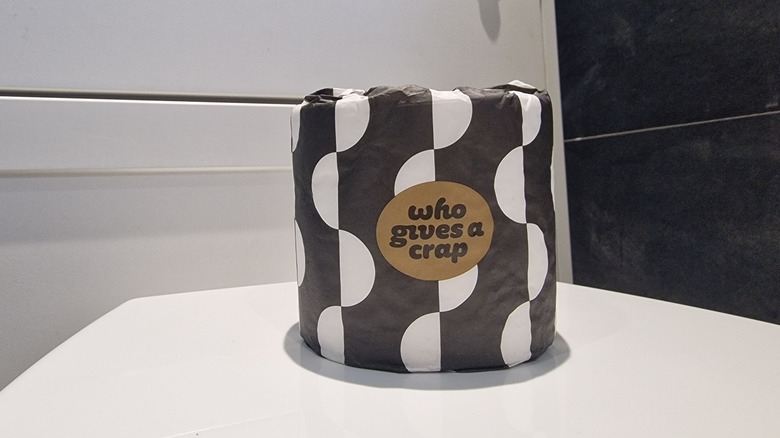A roll of Who Gives a Crap toilet paper wrapped in a black and white package on a white surface