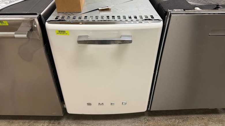 White Smeg STFABWH3 dishwasher in a store or warehouse with stainless steel dishwashers on either side