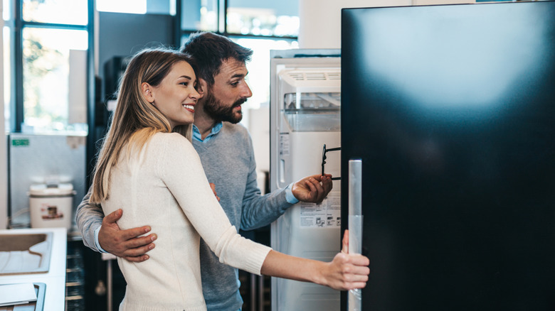 A young couple look at a refrigerator model inside a store.