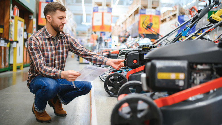 A man in a hardware store trying to choose between a gas and electric lawn mower