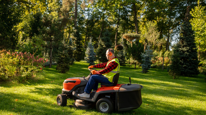 Man uses a riding lawn tractor mower to mow the lawn in his backyard.