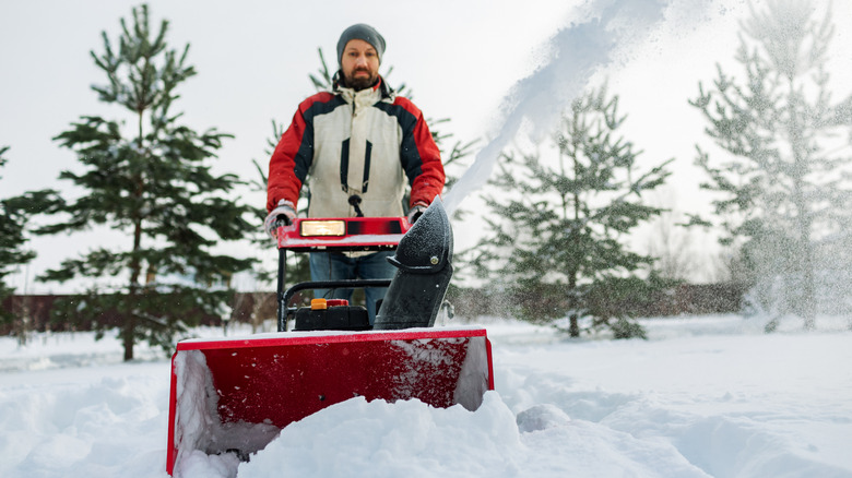 Adult man removing snow with snowblower at backyard of his country house