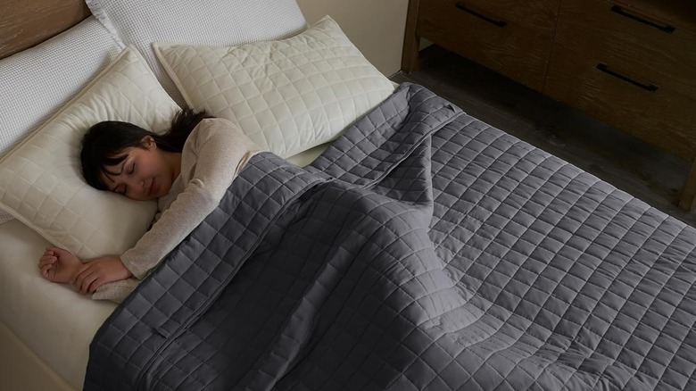Woman lying in bed with YnM Weighted Blanket draped across her
