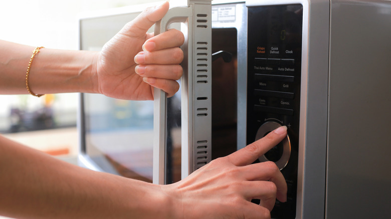 A hand holds the door of a microwave while the other hand pushes the power button.