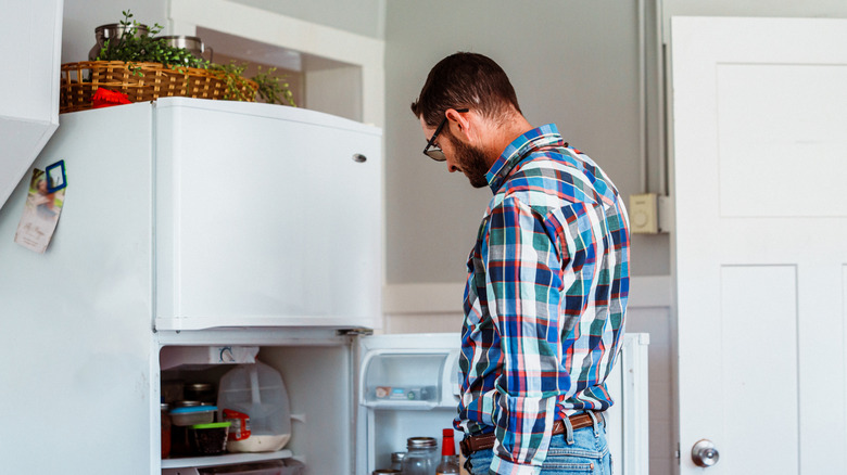 Man looking in a white refrigerator in the garage.