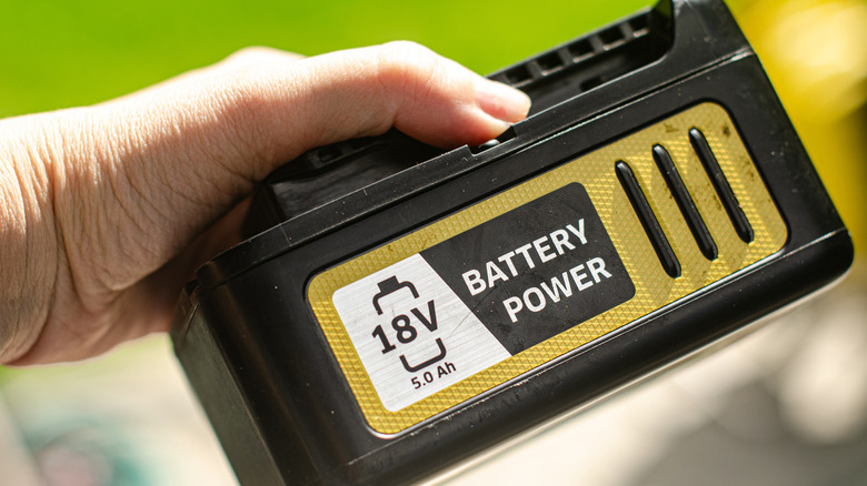 a person holding the battery of an electric cordless lawn mower