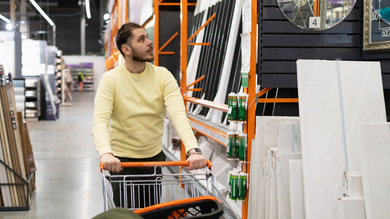 A man pushing a card while browsing the aisles of a home improvement store
