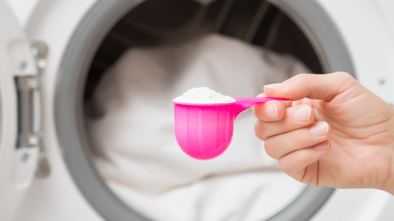 A person holding a pink measuring cup full of powdered laundry detergent.