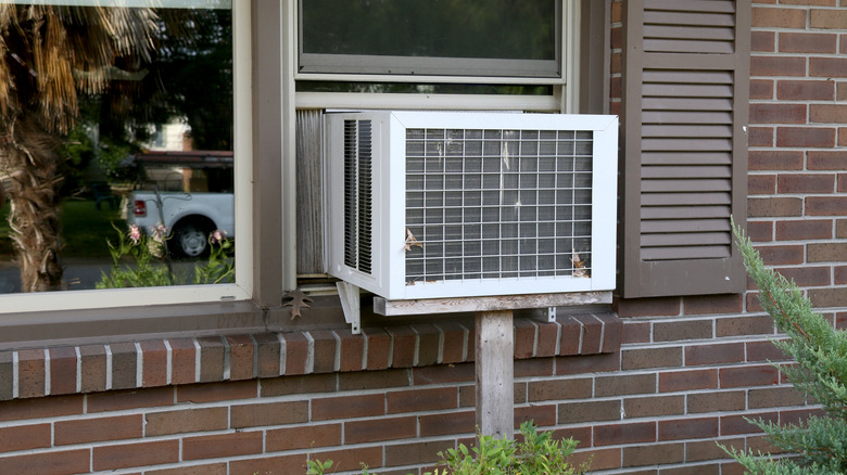 Exterior view of an AC unit in a window with brown shutters on a brick home