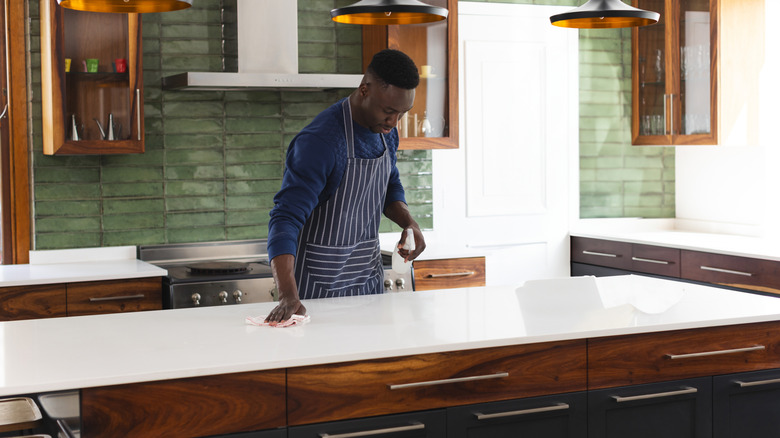 Man wiping white quartz countertop in kitchen with wood cabinetry