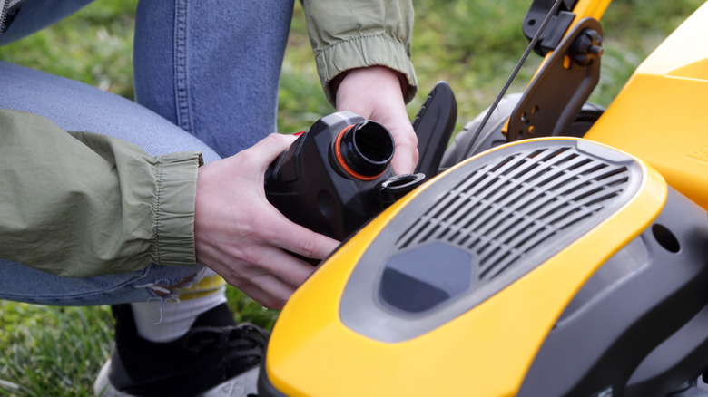 Person fills their lawn mower up with new small engine oil before starting it up for the season.