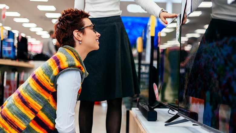 Two people standing by rows of TVs in a store, trying to determine which one they want to buy