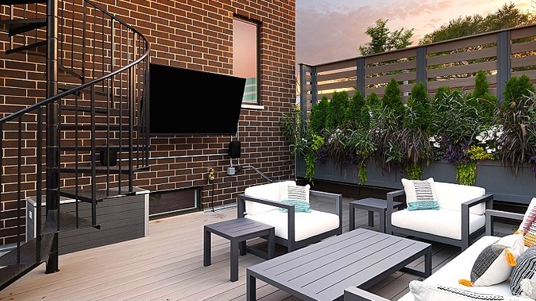 A TV installed outside on a brick wall with patio furniture in front of it