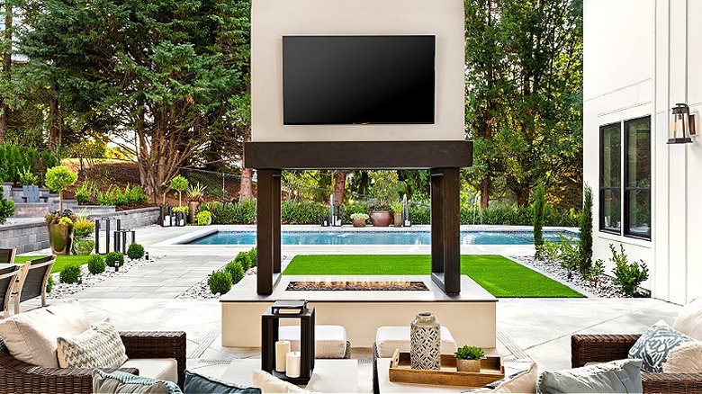 A TV above an outdoor fire pit in front of a pool