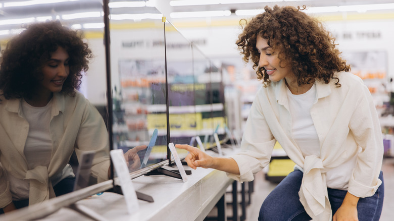 Woman in a light-colored shirt and jeans browsing TVs in a store