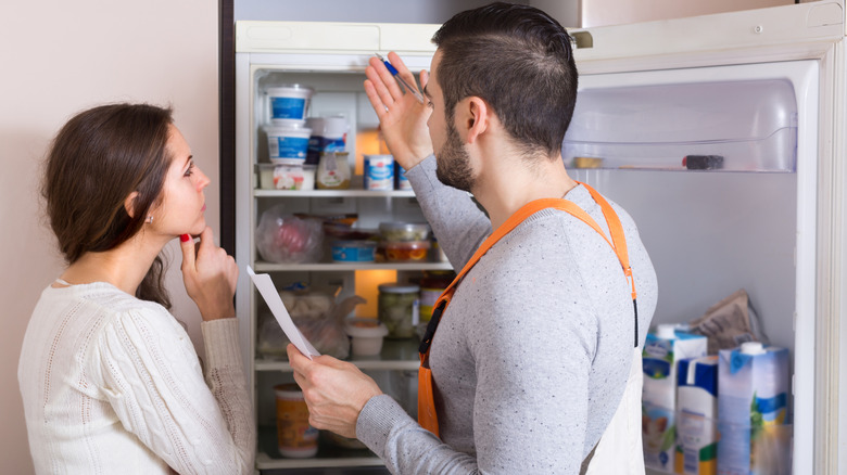A technician talks to a woman about the refrigerator while demonstrating features in her home