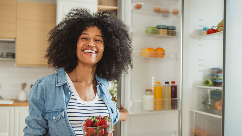 A woman smiles while taking strawberries out of a refrigerator