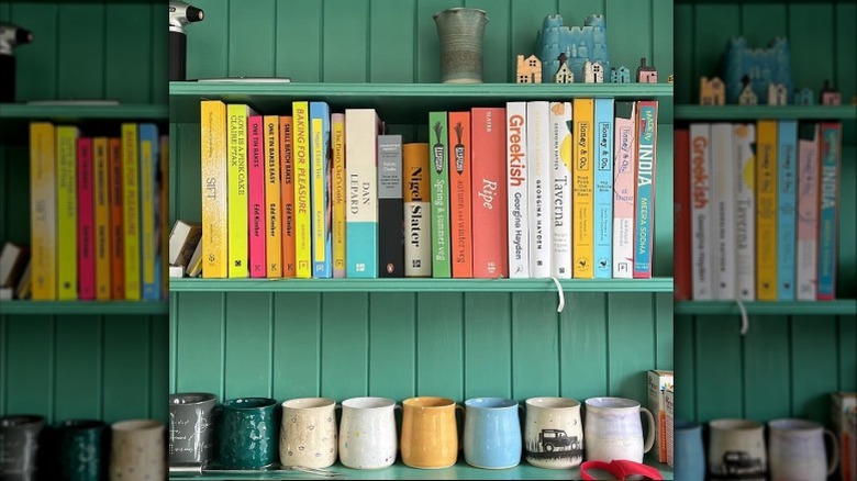 Cookbooks and mugs arranged on a green shelf.