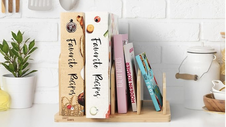 A stack of cookbooks organized in a wooden stand atop a kitchen shelf.