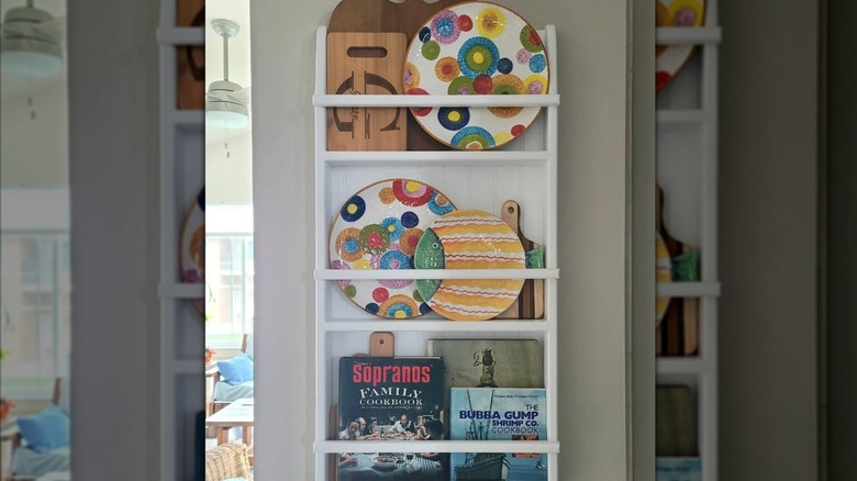 A plate rack displaying colorful plates, cutting boards, and cookbooks.