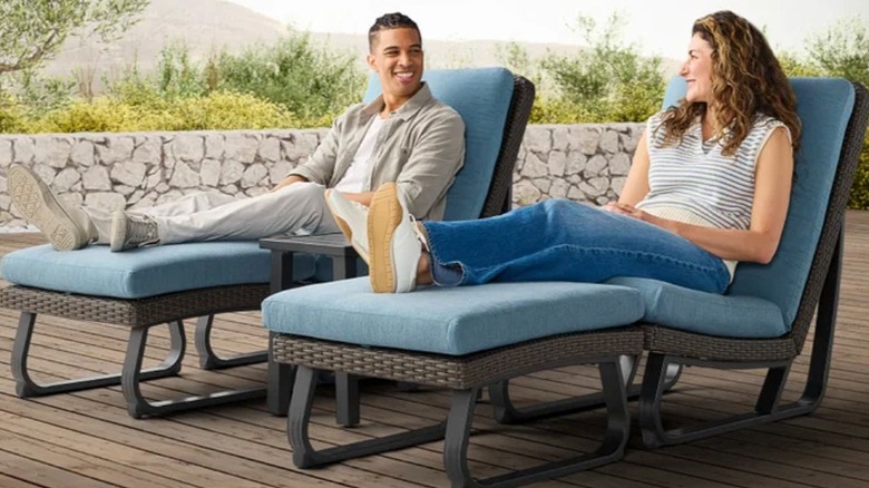 Man and woman sitting on Costco's Agio Trussville patio set with their feet resting on the ottomans