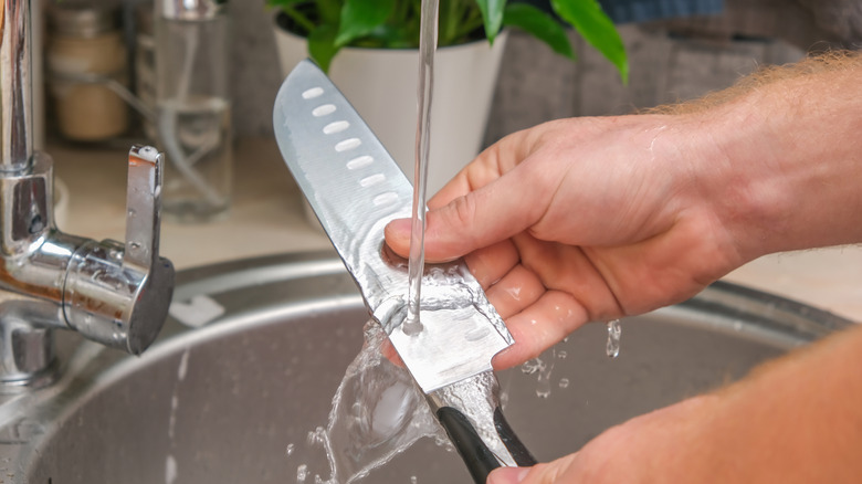 Person rinsing kitchen knife with water in the sink.