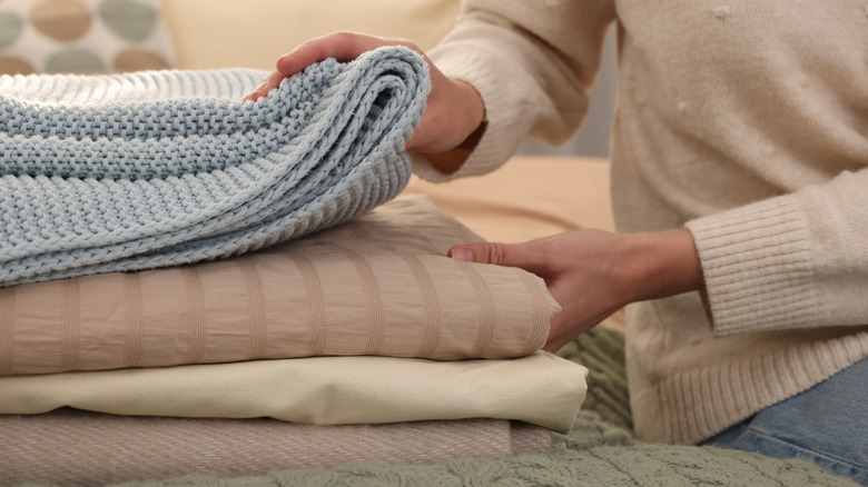 A person sitting on the bed and sorting through a stack of blankets