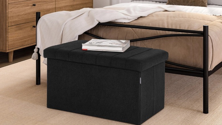 The Seville storage trunk sitting at the base of a bed with a book on top of it