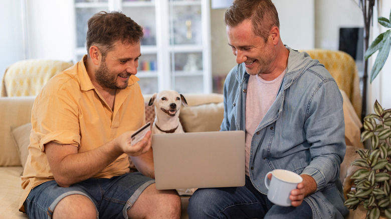 A happy gay couple sitting on a sofa shop online for furniture.